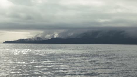 view from calm lake of fog clouds over mountains in british columbia, canada on a moody weather