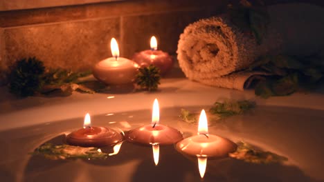 relaxing spa background with candles floating in the bath water, some green petals and a towel near the water surface