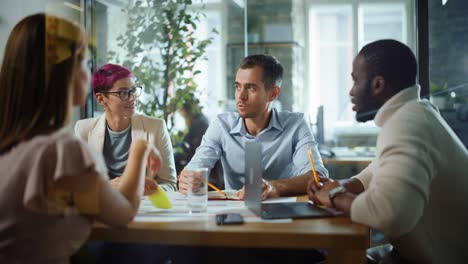 office meeting in conference room: handsome specialist talks about firm strategy with diverse team of professional businesspeople. ambitious, creative start-up team discuss data, design, planning