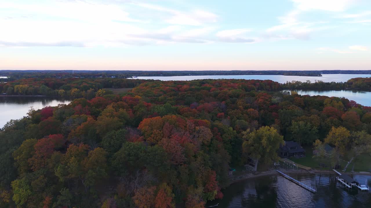 A calm Minnesota afternoon reveals a serene lake surrounded by a forest ablaze with vibrant autumn colors