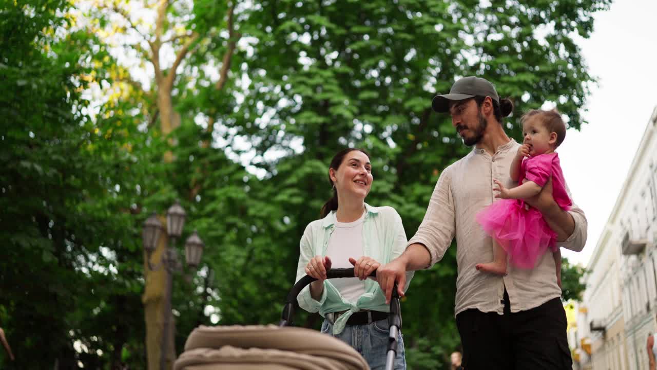 una joven familia camina por una calle de la ciudad, empujando un cochecito y llevando a su bebé