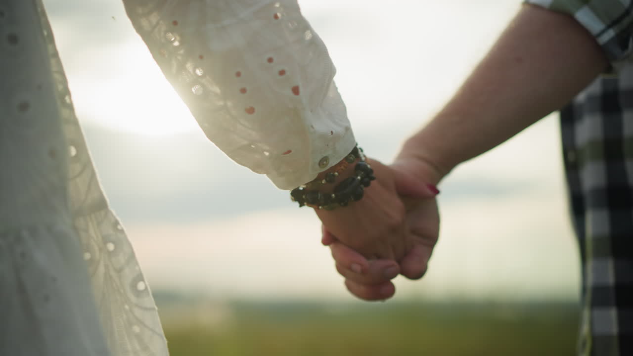 두 손이 서로 부드럽게 붙어있는 클로즈업, 여성의 손은 구슬로 된 팔와 빨간 손으로 장식되어 있습니다. 태양은 배경에서 부드럽게 빛납니다.