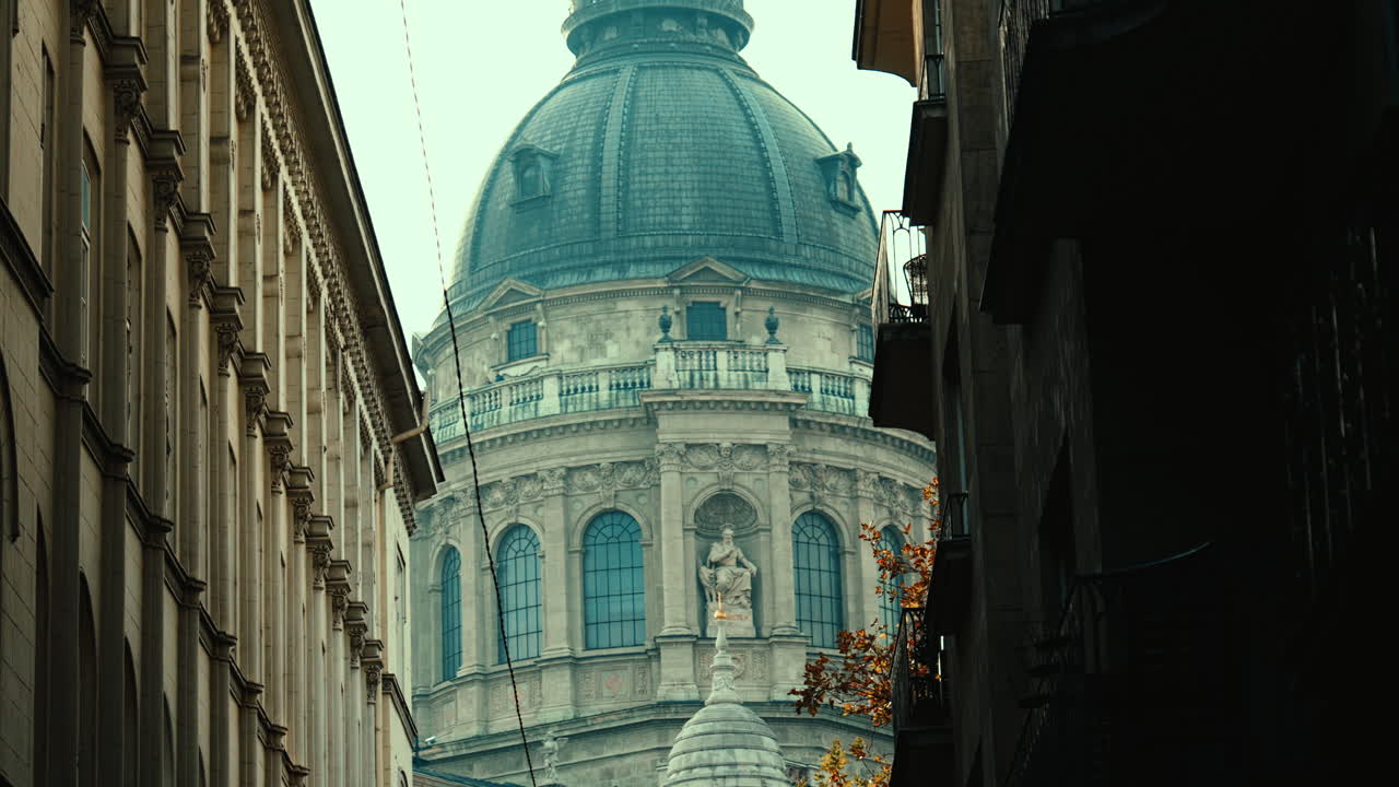St. Stephen’s Basilica framed between two buildings in Budapest, with autumn leaves and warm light creating a cinematic European city atmosphere
