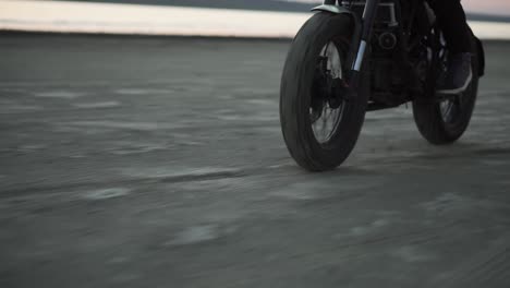 Close-up-of-biker's-ride-on-black-sport-bike-in-helmet-with-switched-front-headlight.-Waterfront,-sunset