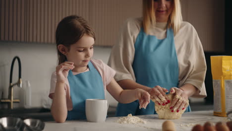 mother and little daughter are baking bread in home woman is kneading dough and child is helping