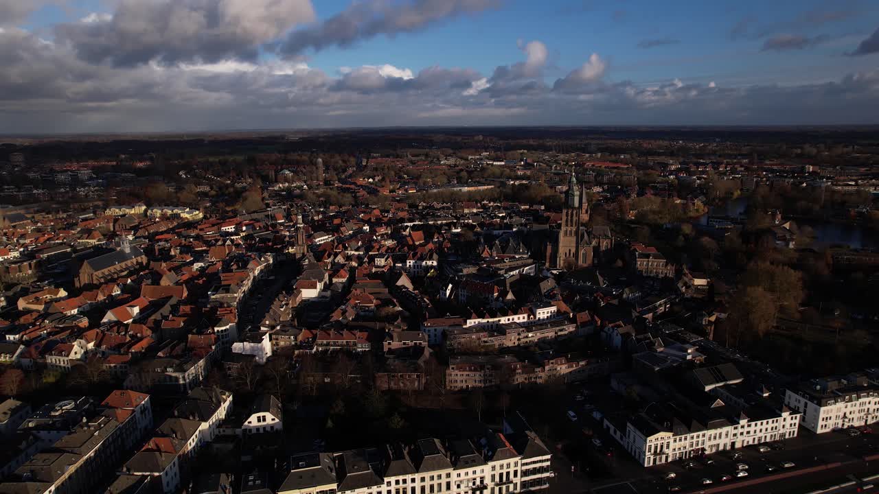 Zoom e avvicinamento aereo sulla storica città di Zutphen con le sue torri, con il panorama urbano visto dall'alto del fiume IJssel, caratterizzato da un forte contrasto di ombre e nuvole drammatiche in alto