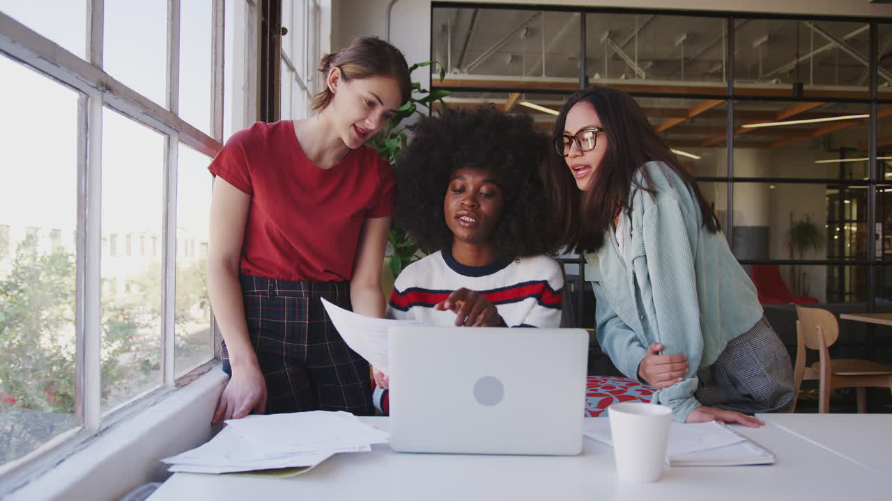 Three millennial women working together  at a desk in a creative office, front view