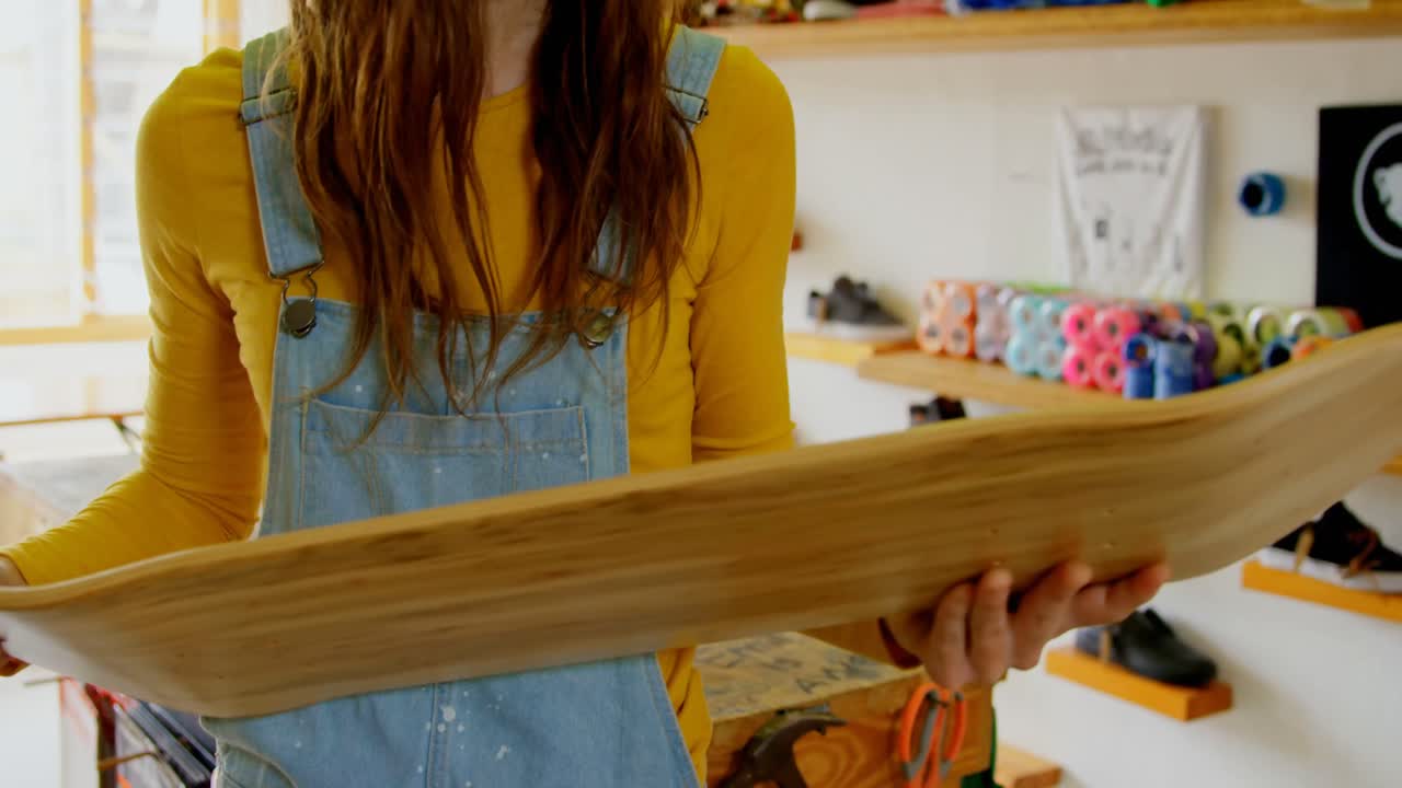 vista frontal de una joven mujer caucásica examinando la cubierta de patinaje en un taller 4k