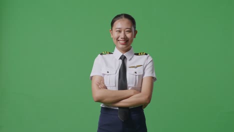 asian woman pilot smiling and crossing her arms to camera while standing in the green screen background studio