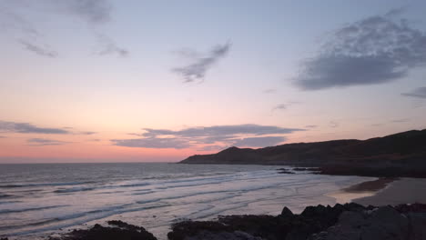 waves crashing against a sandy beach at dusk fading out to the sky in slow motion