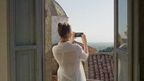 mujer feliz usando un teléfono inteligente tomando fotos disfrutando de compartir experiencias de viajes de vacaciones de verano fotografiando una hermosa vista panorámica en el balcón con gafas de sol