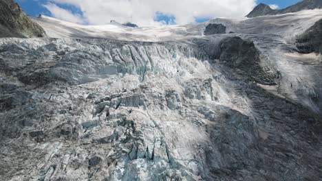 The-moiry-glacier-in-switzerland-on-a-clear-day,-showcasing-rugged-ice-formations-and-snowy-peaks,-aerial-view