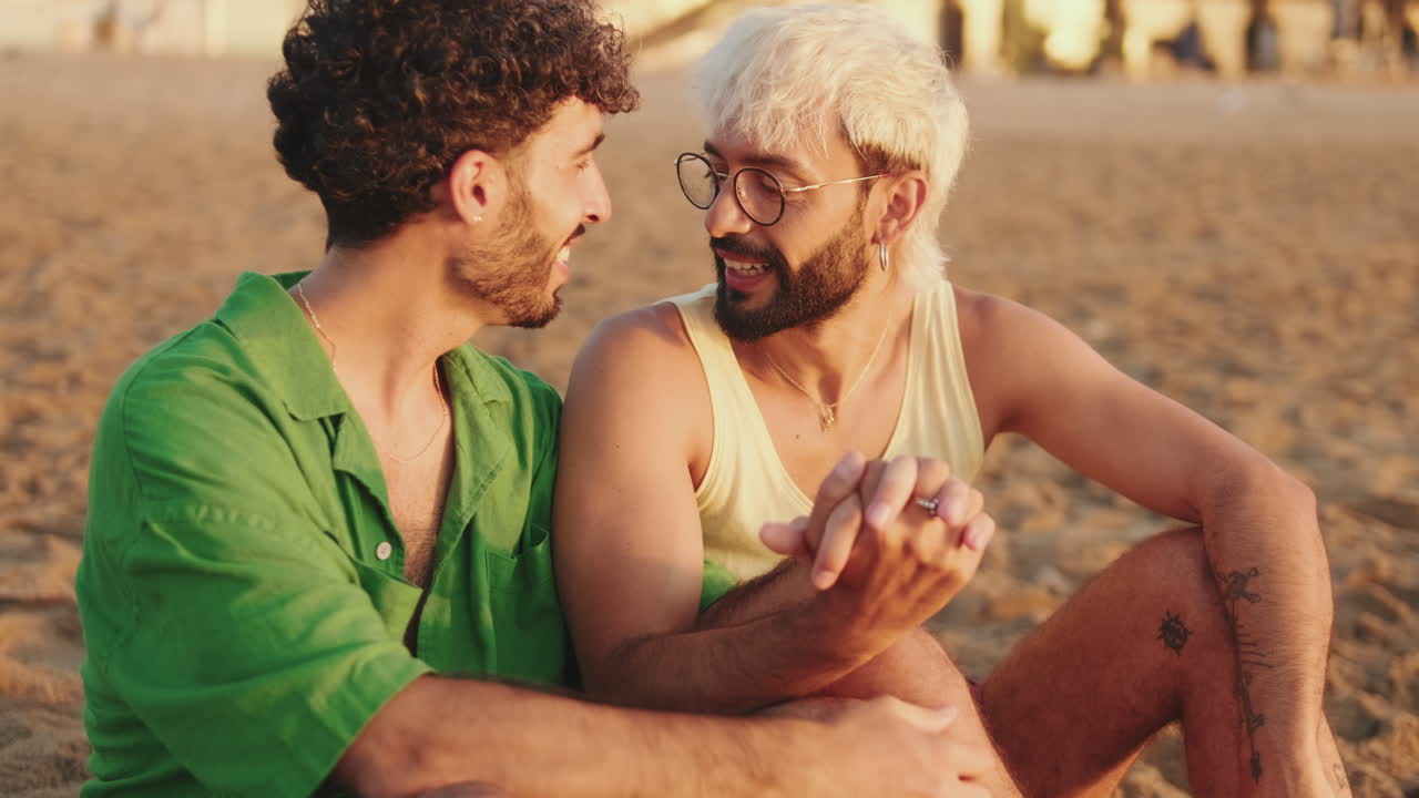 Coppia gay felice che parla e si tiene per mano sulla spiaggia al tramonto