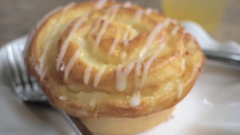 Close-up-footage-of-honey-glazed-roll-on-a-small-porcelain-plate-with-knife-and-fork-on-the-side-revealing-by-zooming-out-and-transitioning-from-deep-focus-to-out-of-focus