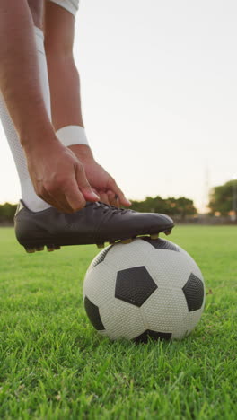 video vertical de un jugador de fútbol biracial en el campo atando los cordones