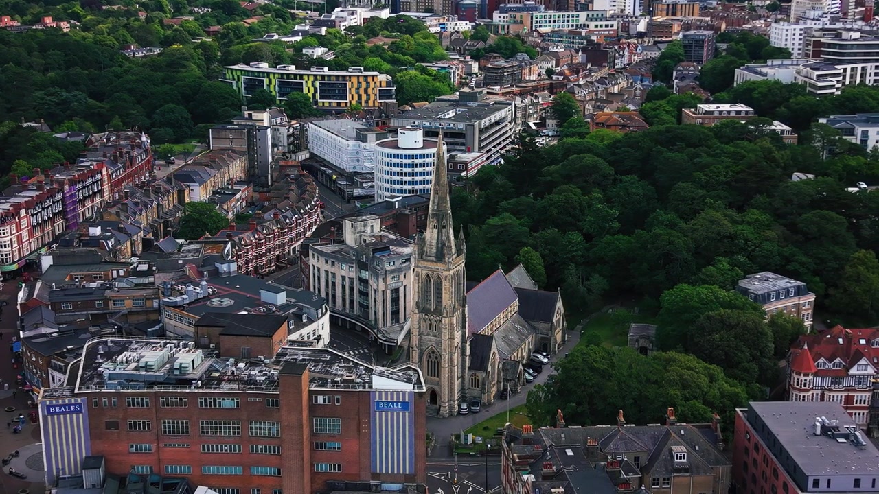 Droneopptak av Bournemouth sentrum som viser et fremtredende kirketårn, historiske bygninger, moderne bebyggelse, hustak, gater og omkringliggende grønne parker. Nyttig for temaer om reiser i Storbritannia