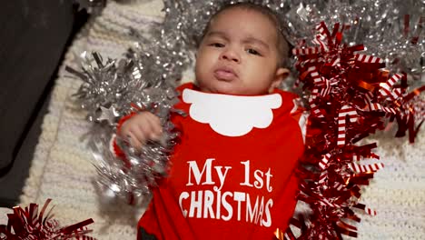 Draufsicht-Auf-Ein-Süßes-Zwei-Monate-Altes-Baby,-Das-Mein-1.-Weihnachtsoutfit-In-Rot-Trägt-Und-Auf-Einer-Decke-Liegt,-Die-Rotes,-Silbernes-Lametta-Zieht-Und-Greift