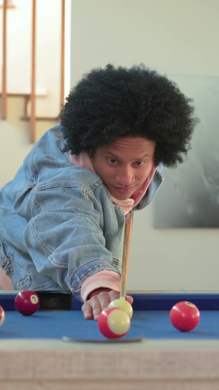 Vertical video: Walking man chalking aiming and hitting ball at home pool table in hoodie for fun