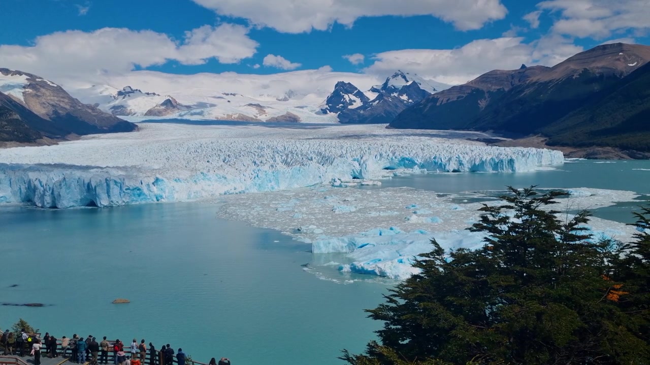 Ampia vista panoramica di turisti che ammirano l'imponente parete di ghiaccio blu del Ghiacciaio Perito Moreno in Patagonia, Argentina, sopra il Lago Argentino turchese, con le Ande innevate sullo sfondo
