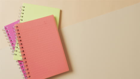 vista aérea de cuadernos de colores con espacio de copia sobre fondo beige, en cámara lenta