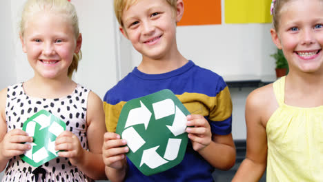 school kids holding recycling symbols and globe in classroom