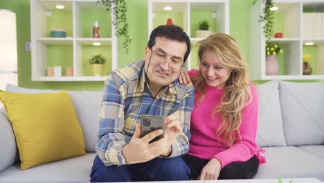 Reifes-Glückliches-Paar,-Das-Zu-Hause-Spaß-Mit-Dem-Smartphone-Hat.-Frau-Und-Mann-Reden,-Lachen.