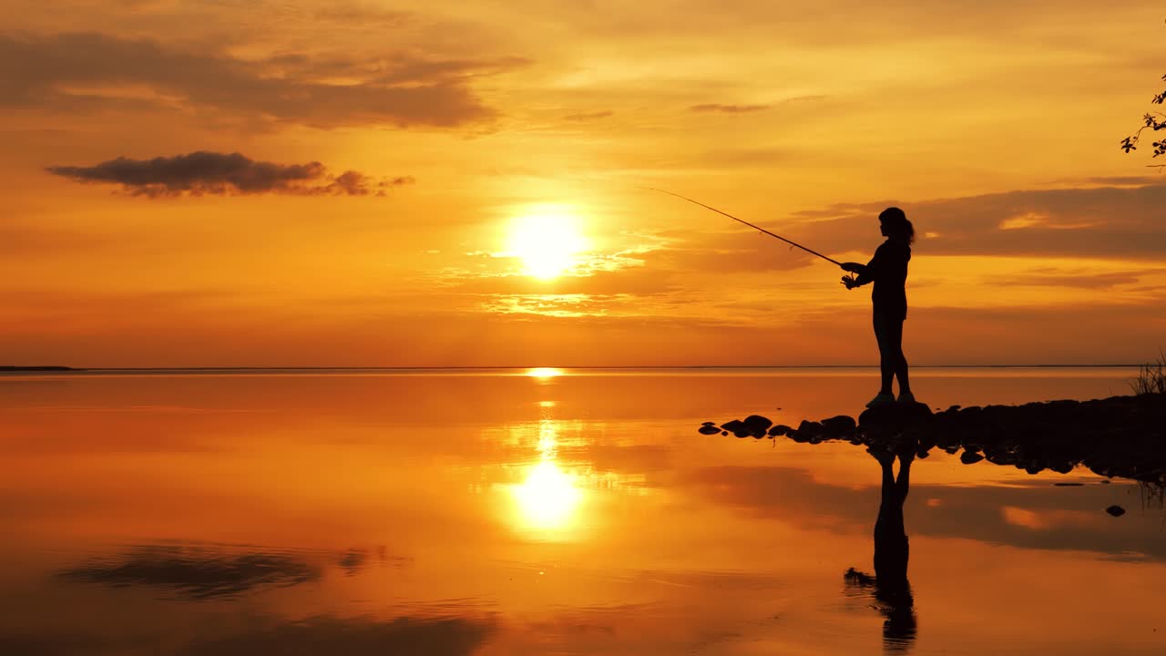 Wanita memancing dengan joran pancing berputar dengan latar belakang matahari terbenam.