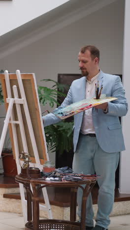 mujer posa para el famoso retratista en el estudio. dama glamurosa en vestido rojo con rosa y maestro de dibujo en la residencia. modelo gracioso con pintor