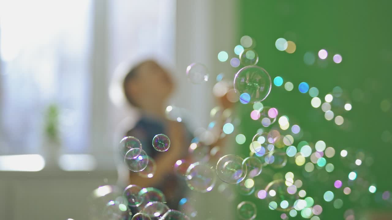 Happy child is playing with soap bubbles at home. A lot of bubble blowers in the air in the room on the background of joyful boy.
