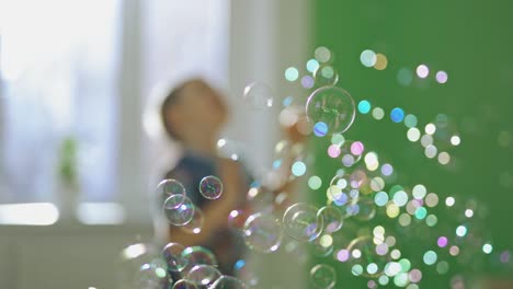 happy child is playing with soap bubbles at home. a lot of bubble blowers in the air in the room on the background of joyful boy.