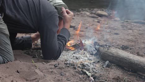 a man blows on a fire on the banks of a river bed in victorias high country