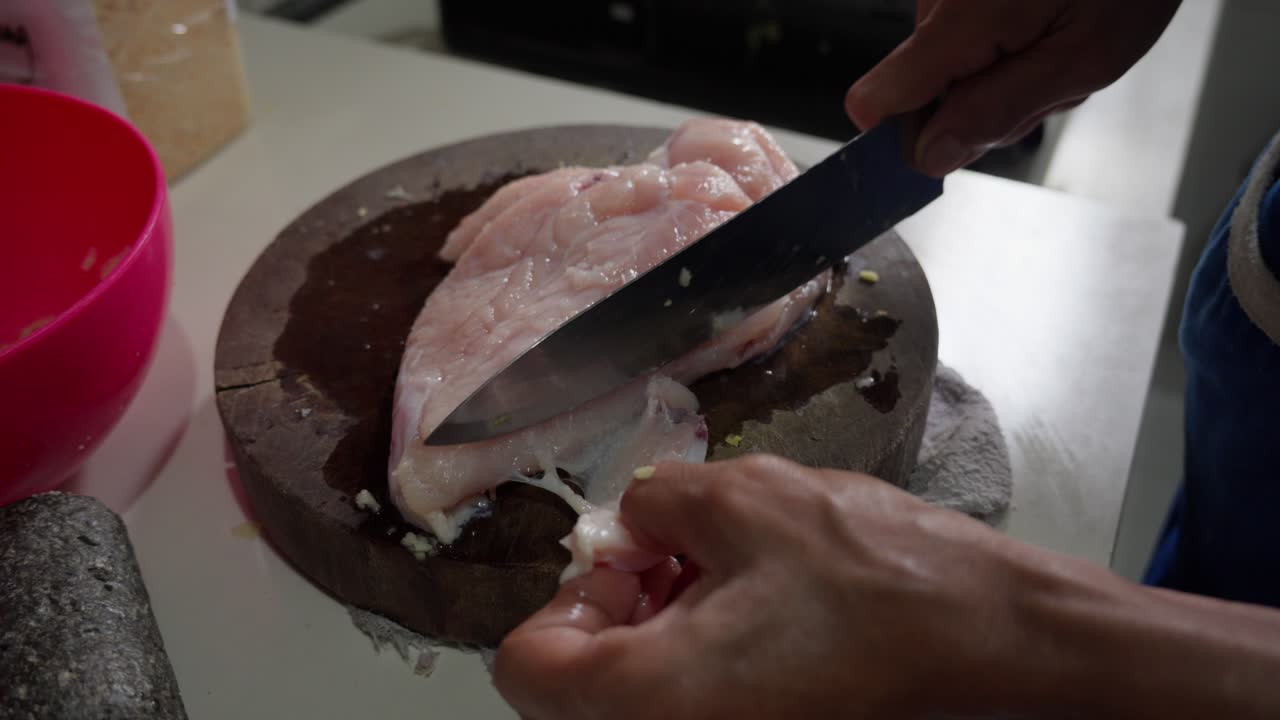 Coltello affilato che taglia pollo crudo su un tagliere rotondo, primo piano