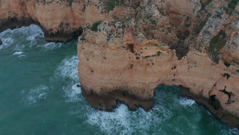 Aerial-drone-tilt-down-above-rocky-cliff-coast-in-Lagos,-Algarve,-Portugal,-birds-eye-overhead-top-down,-windy-day