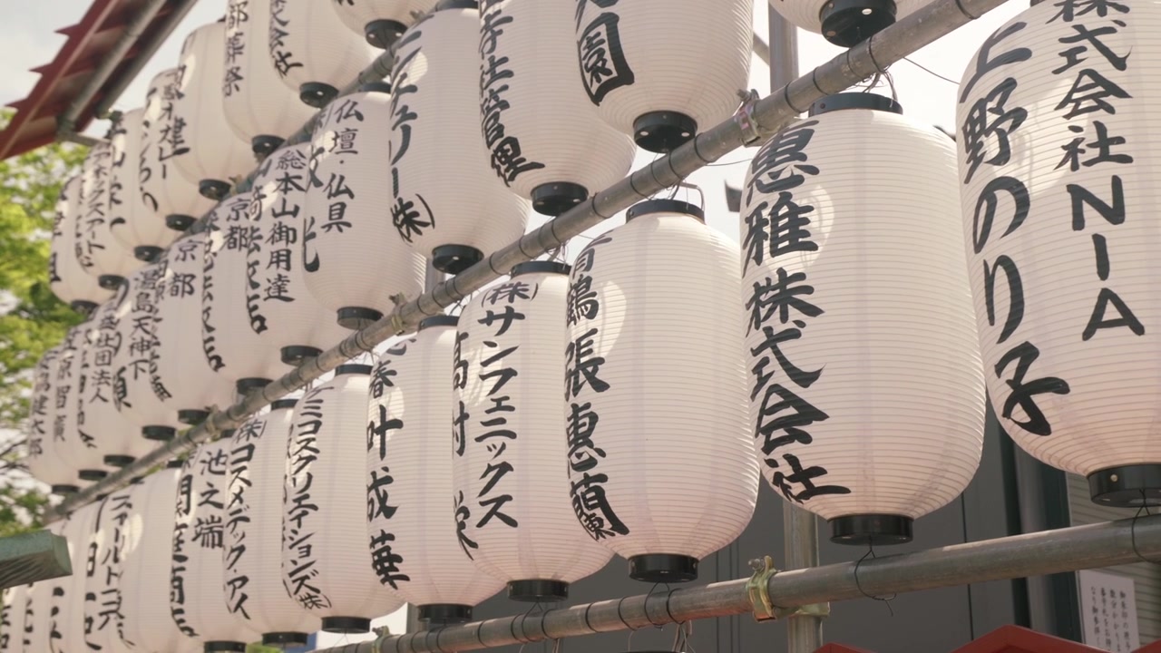Tradiční japonské bílé papírové lucerny (chochin) s černým kaligrafickým písmem visící venku. Detailní záběr.