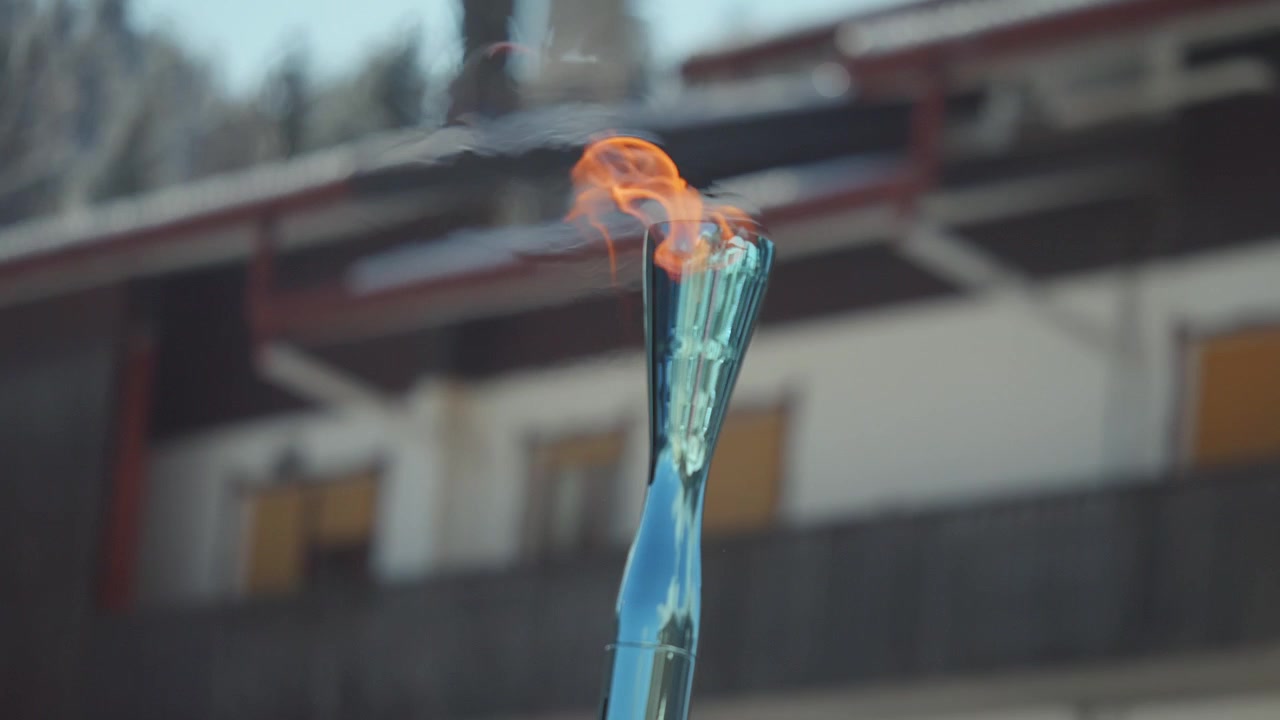 Primo piano di una torcia olimpica con fiamma ardente durante una staffetta nelle Dolomiti. Simbolo sportivo iconico immortalato all'aperto con sfondo morbido e luce naturale