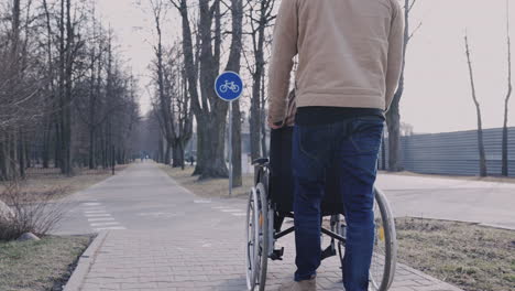 Rear-View-Of-A-Man-Taking-Her-Disabled-Friend-In-Wheelchair-On-A-Walk-Around-The-City