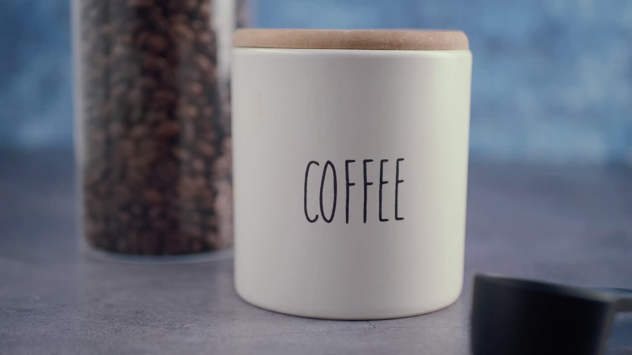 Contenitore bianco per caffè con chicchi di caffè e un misurino.