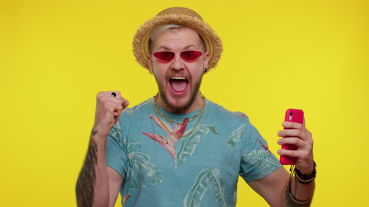 Bearded man tourist with mobile phone celebrating winning holiday resort vacation tickets pass
