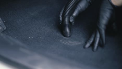 검은 장갑을 끼고 있는 남성의 클로즈업은 검은 실내 차를 진공 청소기로 청소합니다