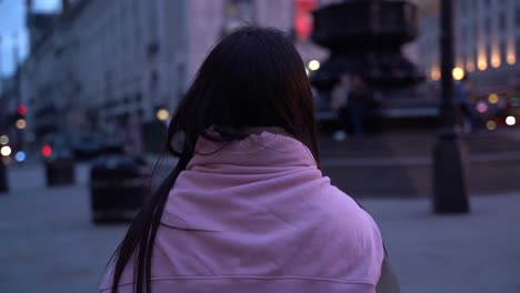 following a young woman at dusk in picadilly circus, london, uk, close up