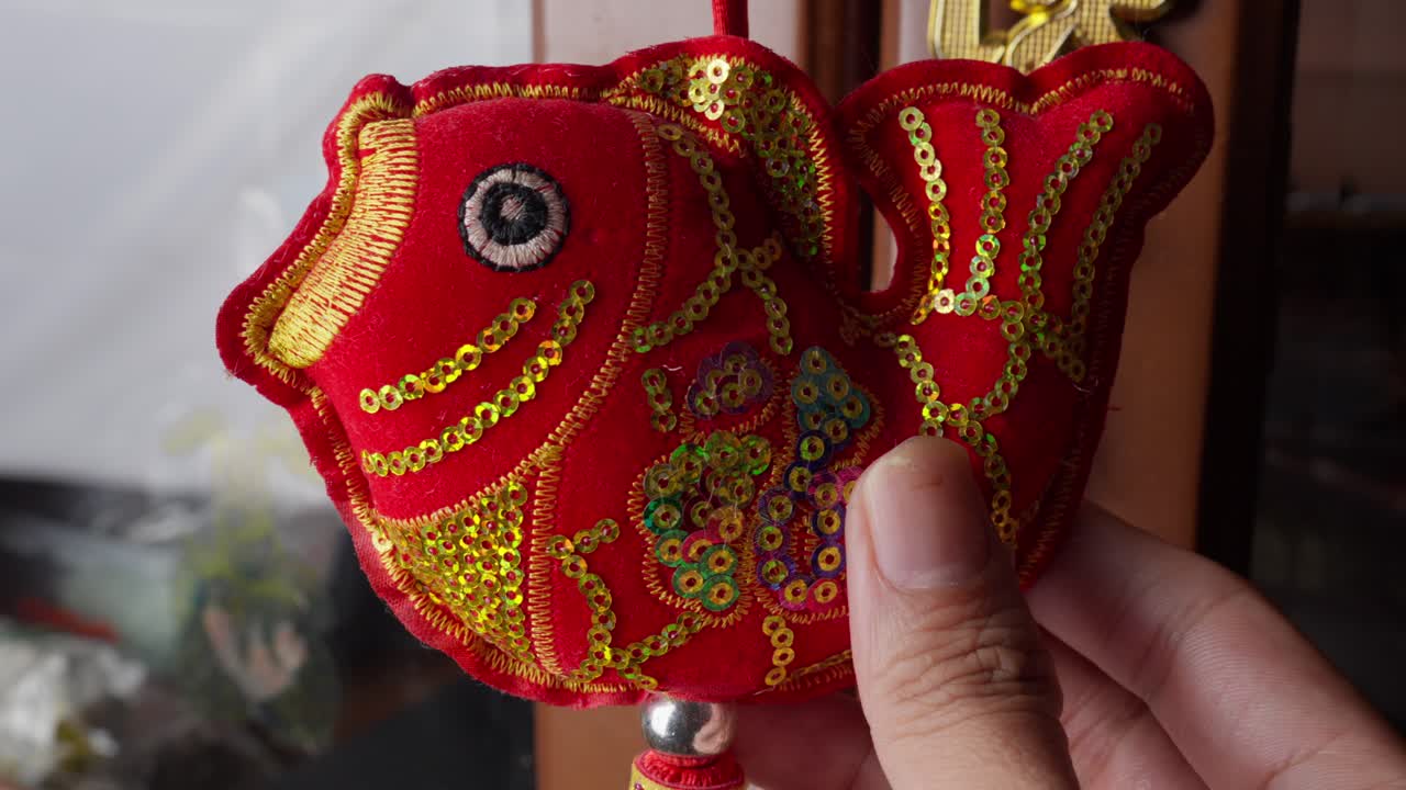 Closeup of a Hand Holding a Red Embroidered Fish Ornament for Chinese New Year