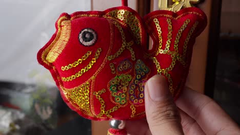 closeup of a hand holding a red embroidered fish ornament for chinese new year