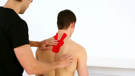 physiotherapist applying red kinesio tape to patients back who gives thumbs up to camera