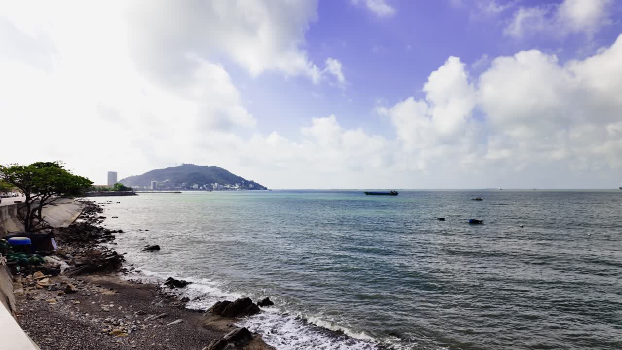 Bai Dua a Vung Tau, Vietnam, mostra persone sulla spiaggia che si godono il sole e l'acqua limpida. Barche si muovono nell'acqua sotto un cielo luminoso.