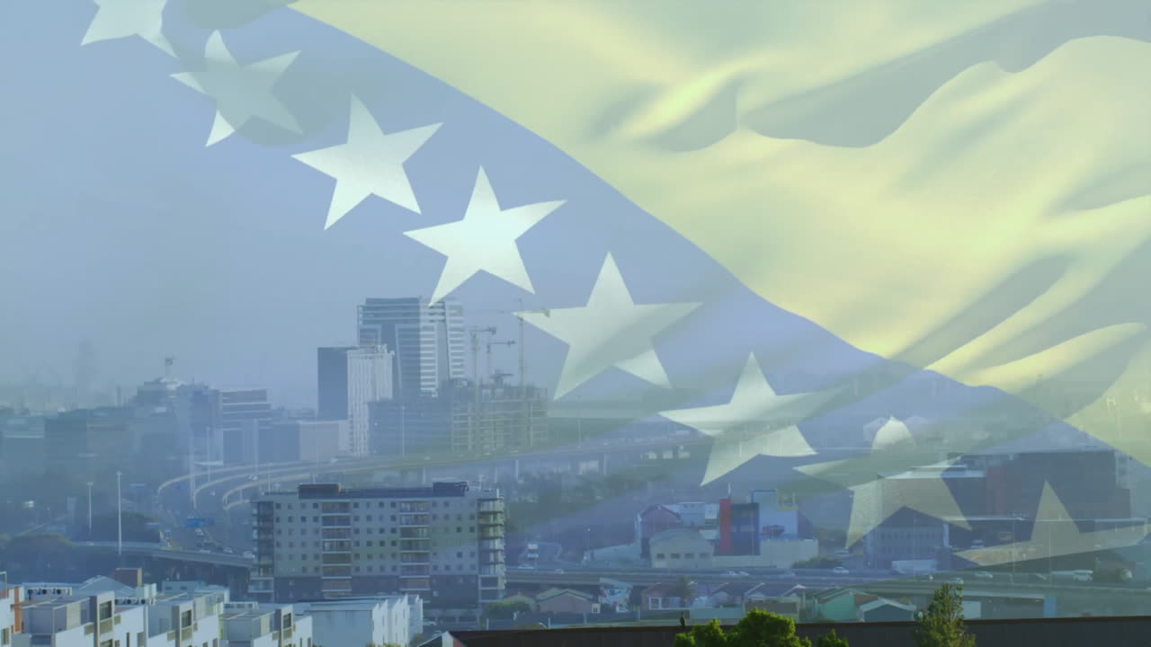 建物と建設クレーンが立ち並ぶ都市の景観の上を舞うボスニア・ヘルツェゴビナ国旗のアニメーション