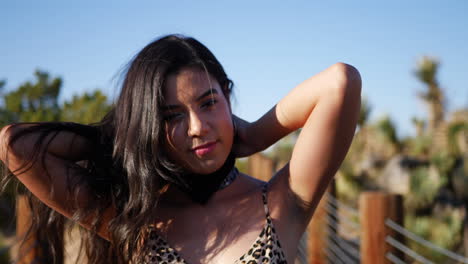 una hermosa joven modelo hispana atando un pañuelo y mirando con una sonrisa en un paisaje desértico al aire libre a cámara lenta
