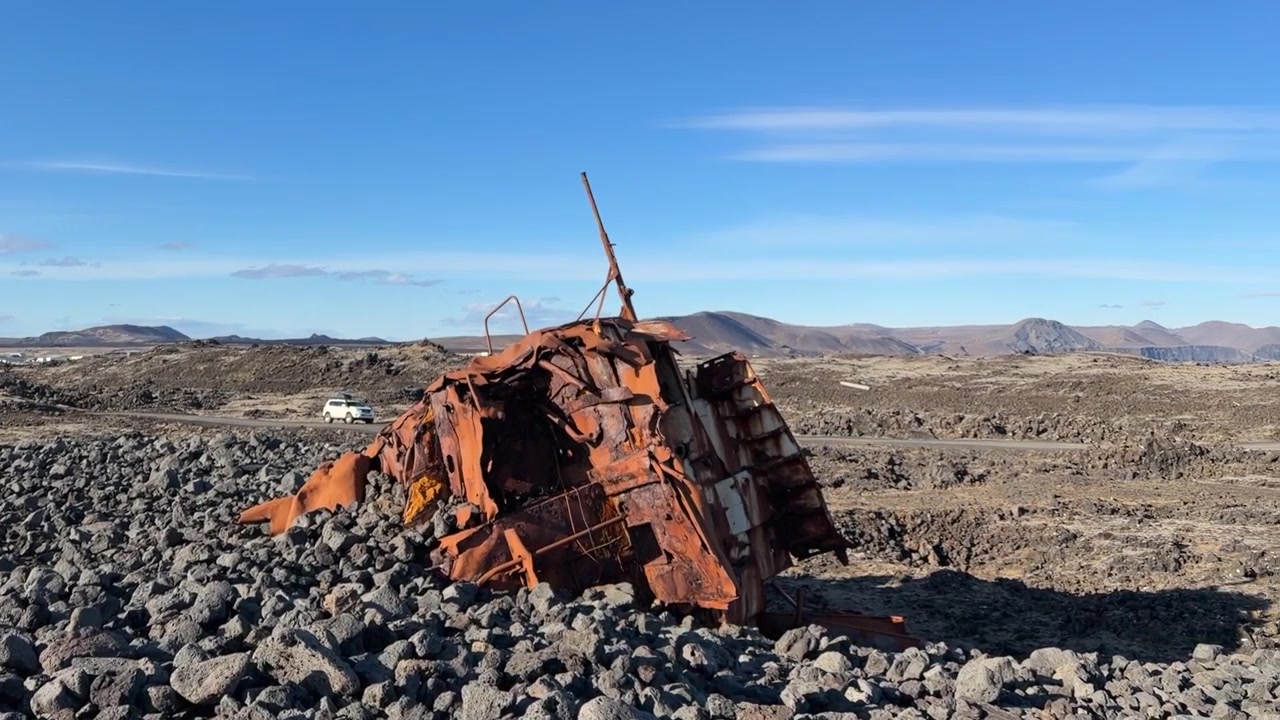 Et gammelt rustent skipsvrak begravd på den steinfylte stranden nær Grindavik, Island, skinner i solen på en nydelig klarværsdag i ildens og isens land