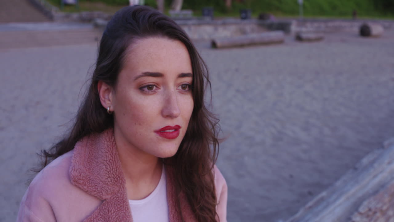 una hermosa mujer joven se sienta en una playa y observa la puesta de sol sobre el océano