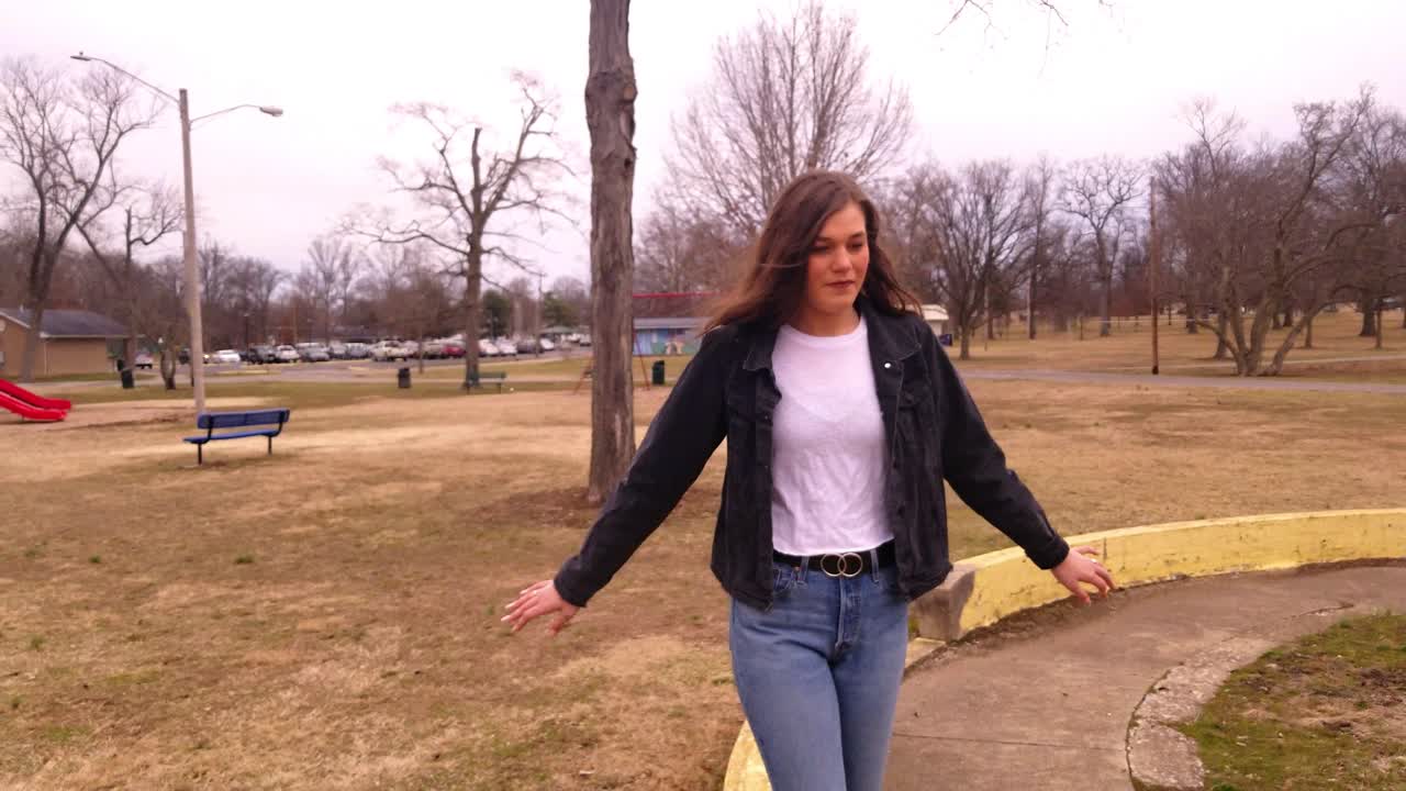 imágenes en 4k de una hermosa adolescente universitaria morena caminando sobre una plataforma elevada de concreto mientras intenta mantener el equilibrio
