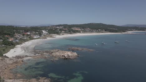 raw aerial shot of rocky shore and beach with clear water with sailboats